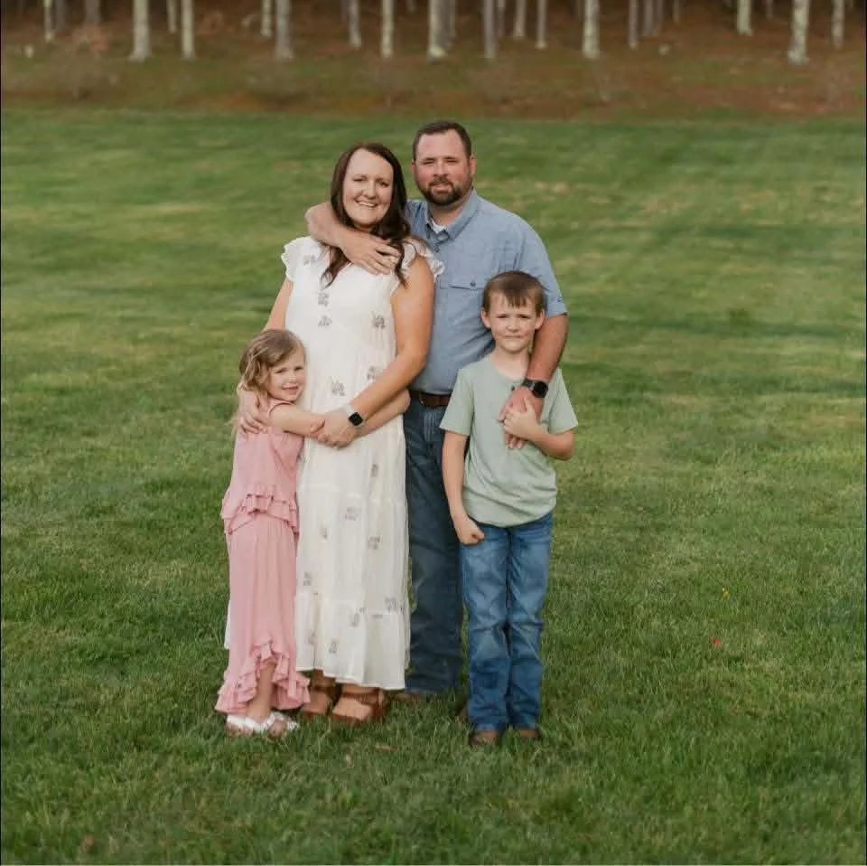 Josh with his wife and their two children, standing together in a grassy field